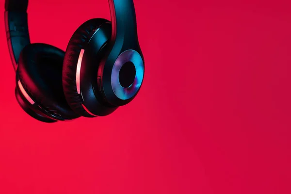 Close-up shot of retro 90s style photo of black stylish modern wireless headphone in neon lights over red background. — 图库照片