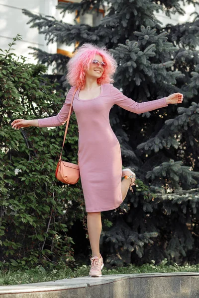 Jovem encantadora com cabelo rosa encaracolado e óculos de sol perto da árvore de primavera florescente . — Fotografia de Stock
