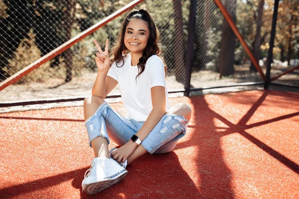 Feliz morena joven con sonrisa brillante vestida con ropa casual moderna posando en el estadio . — Foto de Stock