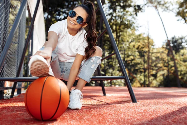 Snygg brunett ung kvinna klädd i avslappnade moderna kläder poserar med basket på arenan. — Stockfoto