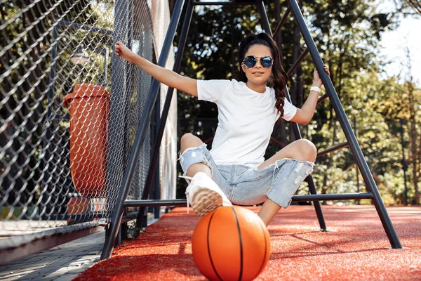 Modern kıyafetler giymiş, stadyumda basketbolla poz veren sevimli genç bir kadın.. — Stok fotoğraf