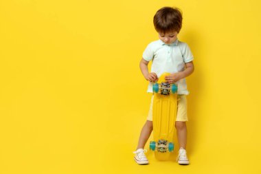 Sarı arka planda elinde pennyboard ya da kaykay tutan sıradan yaz kıyafetli şirin bir çocuk..
