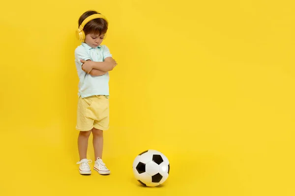 全长照片，照片上的小男孩头戴耳机，头戴黄色背景的足球. — 图库照片