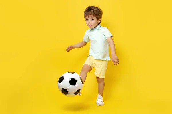 穿着休闲夏装的可爱小孩儿在黄色背景下与足球玩耍. — 图库照片