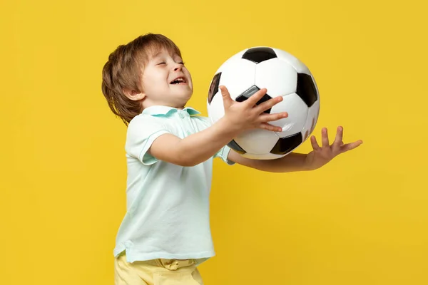 穿着休闲装的滑稽小女孩试图用黄色的背景接住足球. — 图库照片