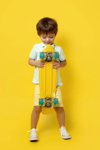 迷人的小男孩穿着休闲装，手持黄底的铅笔板或滑板. — 图库照片