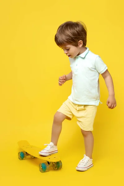 迷人的小男孩穿着休闲的夏装，在黄色的背景上玩铅笔板或滑板. — 图库照片