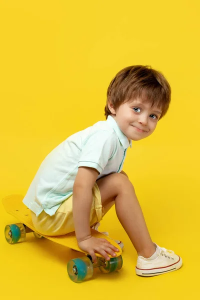 迷人的小男孩穿着休闲装，坐在滑板上或黄色背景的滑板上. — 图库照片