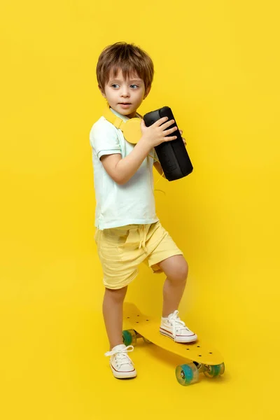 在黄色背景的便携黑色无线扬声器上听音乐的可爱孩子的全长照片. — 图库照片
