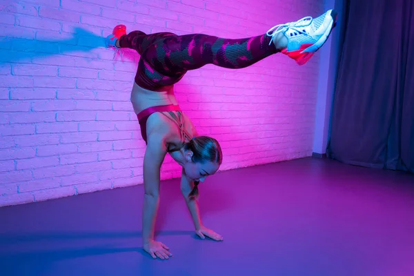 在霓虹灯的砖墙上伸展着年轻女子体操运动员的运动服. — 图库照片
