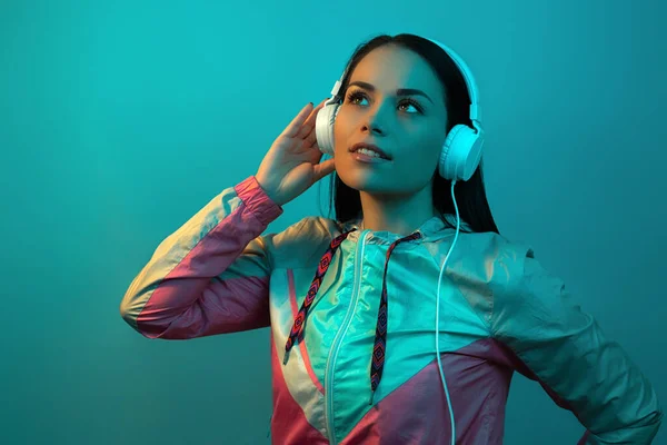 Ładna młoda kobieta z białymi słuchawkami słuchająca muzyki w neonach w studio. — Zdjęcie stockowe