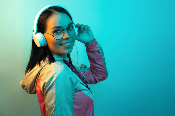 Ładna młoda kobieta z białymi słuchawkami słuchająca muzyki w neonach w studio. — Zdjęcie stockowe