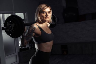 Genç, sarışın kadın spor salonunda halter egzersizi yapıyor..