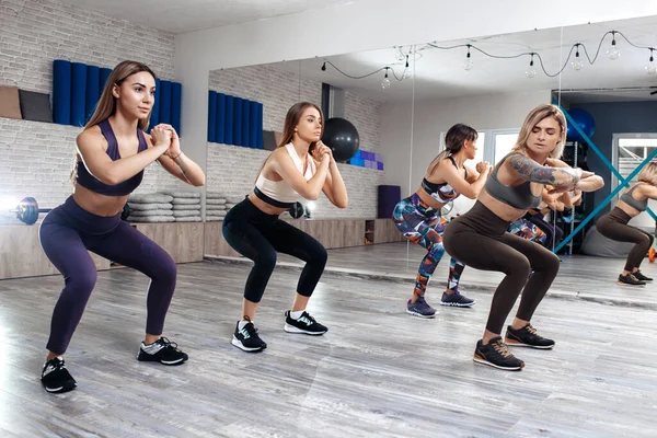 Gruppe von vier jungen motivierten Mädchen beim Kniebeugen im Fitnesskurs. Sport, Fitness und Lifestylekonzept. — Stockfoto