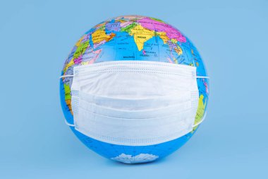 Mavi arka planda antiviral cerrahi koruyucu yüz maskesi olan dünya küresi modeli. Dünya gezegeni konseptini koru.