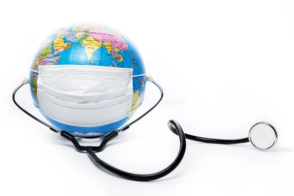 Globe terrestre avec masque chirurgical antiviral et stéthoscope sur fond blanc. Protéger le concept de planète . — Photo