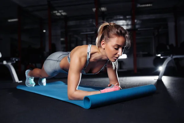 Spor giyimli genç bir kadın spor salonundaki spor salonunda ya da yoga sınıfındaki spor minderinde tahta egzersizi yapıyor. Sağlık kavramı. — Stok fotoğraf