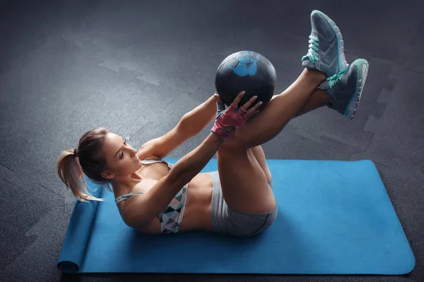 Fit jonge vrouw doen sit-ups buikspieren crunches kern oefeningen met medicinale bal. — Stockfoto