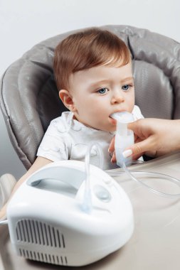 Anne, sandalyede oturan sevimli bebek için nebulizör kullanıyor. Sağlık hizmeti kavramı.