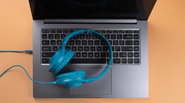 Modern bilgisayar ya da dizüstü bilgisayar ve bej arka planda mavi kulaklık fotoğrafı. Yakın plan..