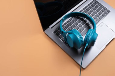 Modern bilgisayar ya da dizüstü bilgisayar ve bej arka planda mavi kulaklık fotoğrafı. Yakın plan..