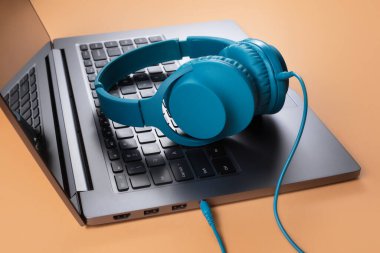 Modern bilgisayar ya da dizüstü bilgisayar ve bej arka planda mavi kulaklık fotoğrafı. Yakın plan..