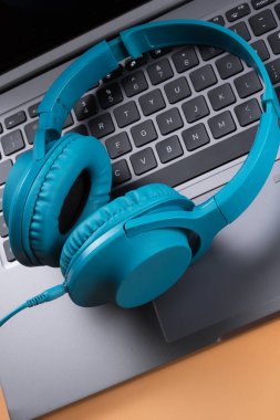 Modern bilgisayar ya da dizüstü bilgisayar ve bej arka planda mavi kulaklık fotoğrafı. Yakın plan..