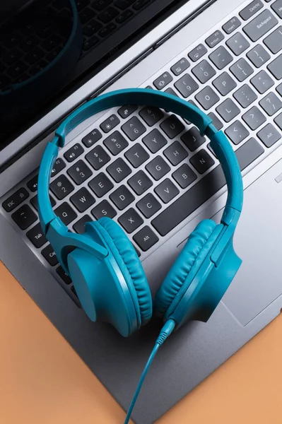 Photo of stylish modern computer or notebook and blue cyan headphones over beige background. Close-up. — Stock Photo, Image
