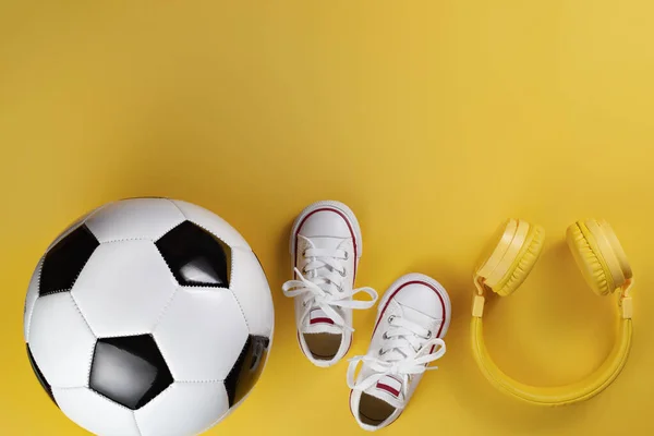 黄色耳机、白色运动鞋和传统足球风格在黄色背景下的特写照片. — 图库照片