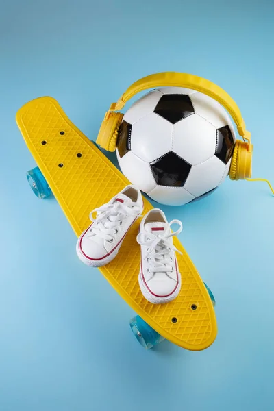 蓝色背景的黄色耳机、白色运动鞋和传统风格的足球. — 图库照片