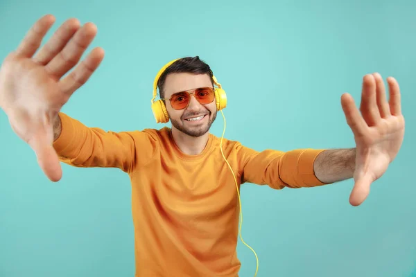 Απρόσεκτος γενειοφόρος νεαρός άνδρας που φοράει γυαλιά ηλίου ακούγοντας μουσική και χορεύοντας σε κυανό φόντο. — Φωτογραφία Αρχείου