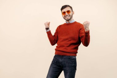 Günlük kıyafetli, güneş gözlüklü, bej arka planda kutlama yapan hoş sakallı adam. Başarı ve kazanan.