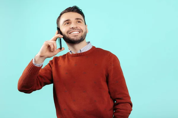 Vrolijke bebaarde jongeman in casual outfit praten op smartphone over cyaan achtergrond. — Stockfoto