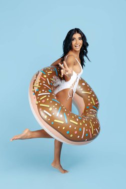 Mayo giymiş çekici genç bir kadın mavi arka planda donut şişirilebilir halkayla poz veriyor..