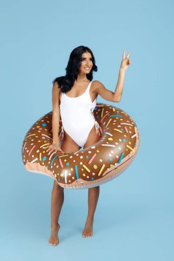 Mayo giymiş sağlıklı bir kadın. Donutla mutlu poz veriyor. Şişirilebilir..