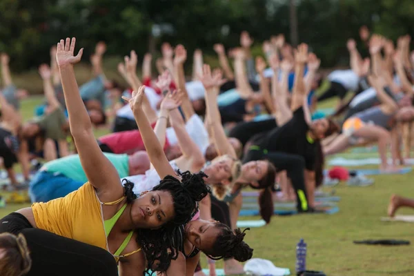 Docenas de personas hacen la postura del triángulo en la clase de yoga al aire libre —  Fotos de Stock