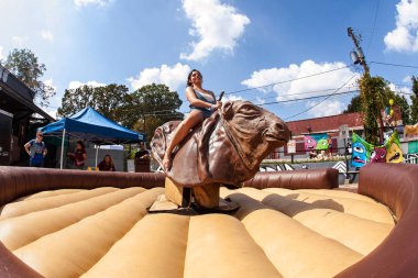 Woman Tries To Stay Upright Riding Mechanical Bull At Festival clipart