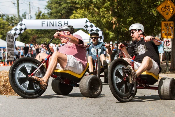 Men Riding Adult Big Wheels Race Each Other At Festival — Stock Photo, Image