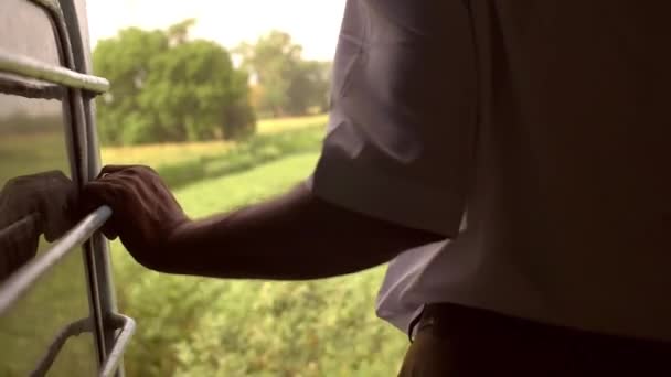 Mann hält sich an Geländer eines Zuges, der durch Felder fährt — Stockvideo