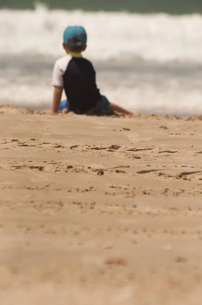 Deniz izlerken kum üzerine oturan küçük bir çocuk