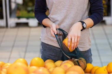 Bir kadın portakalları tekrar kullanılabilir bir çantaya koyar..