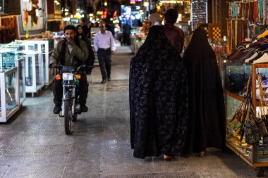 İsfahan, İran - Kasım 2019. Chador 'da iki kadın Doğu Çarşısı' na gidiyor. Karşısında motosiklet süren bir adam var..