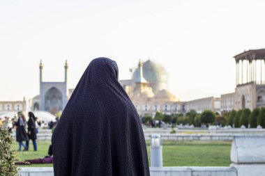 Naghsh-e Cihan Meydanı 'ndaki Şah Camii' ne (Yeni Abbasi Camisi veya Kraliyet Camisi olarak da bilinir) bakan siyah çarşaflı kadın görülüyor. Arka plan.