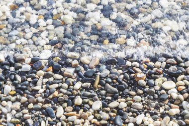 Deniz kıyısı renkli çakıl taşlarıyla kaplı. Yumuşak şeffaf dalga, deniz arka planı.