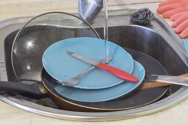 Pile of dirty dishes in a sink in kitchen. Water flows from the tap.