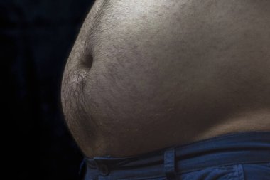 Siyah arka planda karanlık ışık altında bir adamın karnı. Merkezi obez bir erkek..
