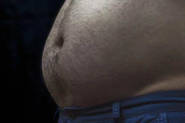 Belly of a man in dark light on black background. A centrally obese male.