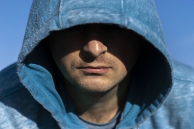 Mavi kapüşonlu adam. Arka planda kapüşonlu bir adamın portresini yakından çek. Tanımlanamayan bir yüz gölgede saklı..