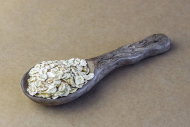 Kahverengi kağıt masa örtüsü üzerinde seramik kaşıkta pişmemiş yulaf ezmesi..