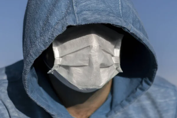 An unrecognizable male face is hidden by a hood and a medical mask. Close-up portrait.